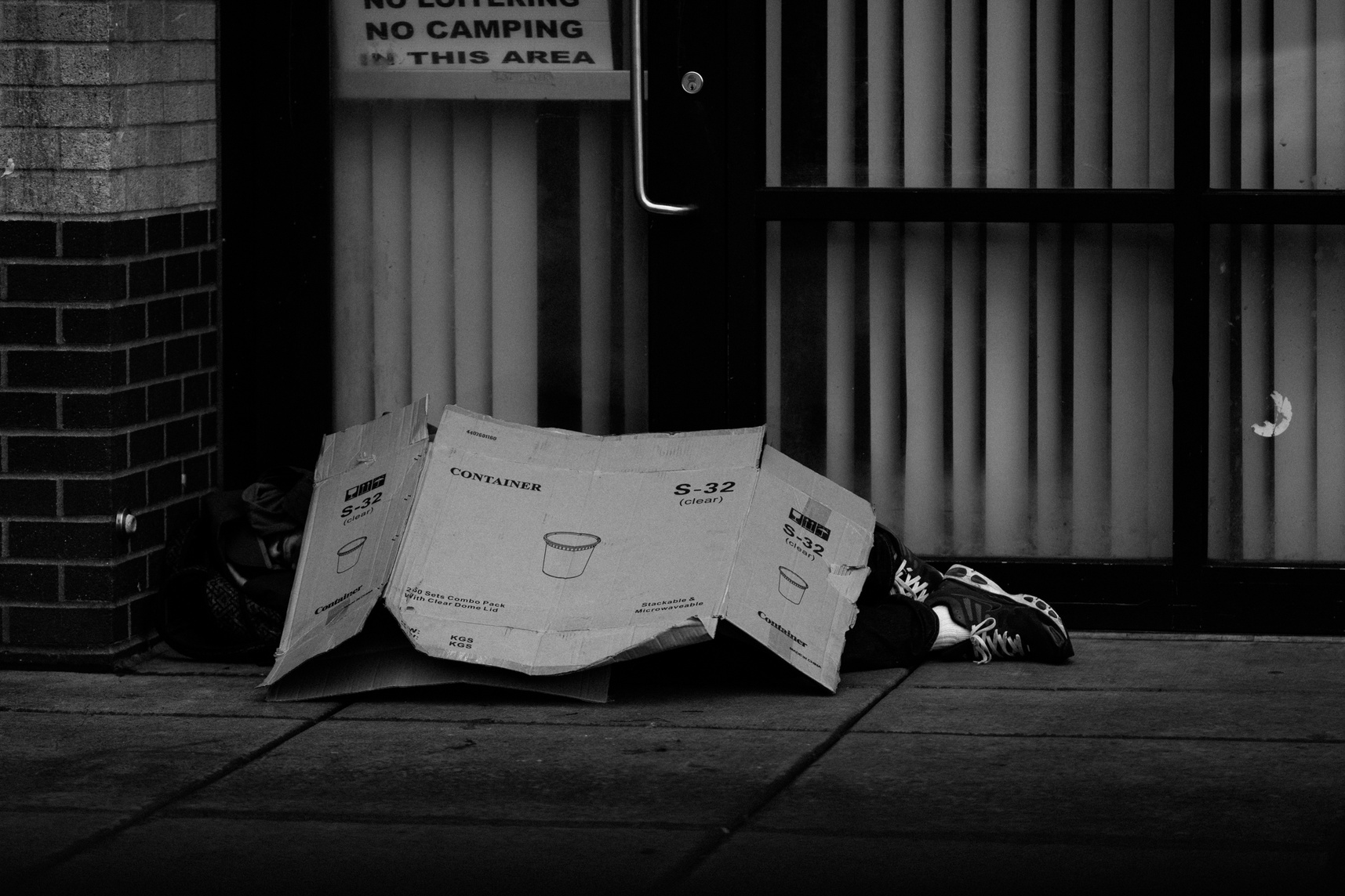 Grayscale Photo of Human Lying on Ground Covered of Cardboard Box